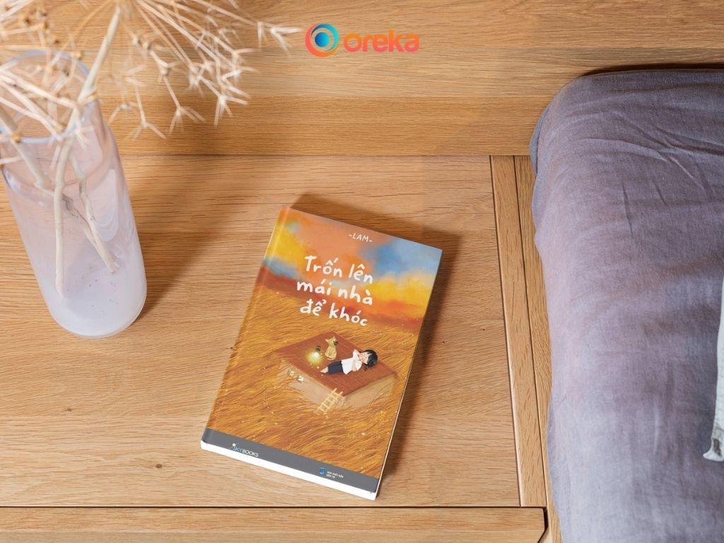 Trốn Lên Mái Nhà Để Khóc: Một Cuốn Sách Chữa Lành Nên Đọc 1 sách Trốn lên mái nhà để khóc review. Hình ảnh cuốn sách được đặt cạnh tủ gỗ đầu giường, bên cạnh có một bình hoa khô.