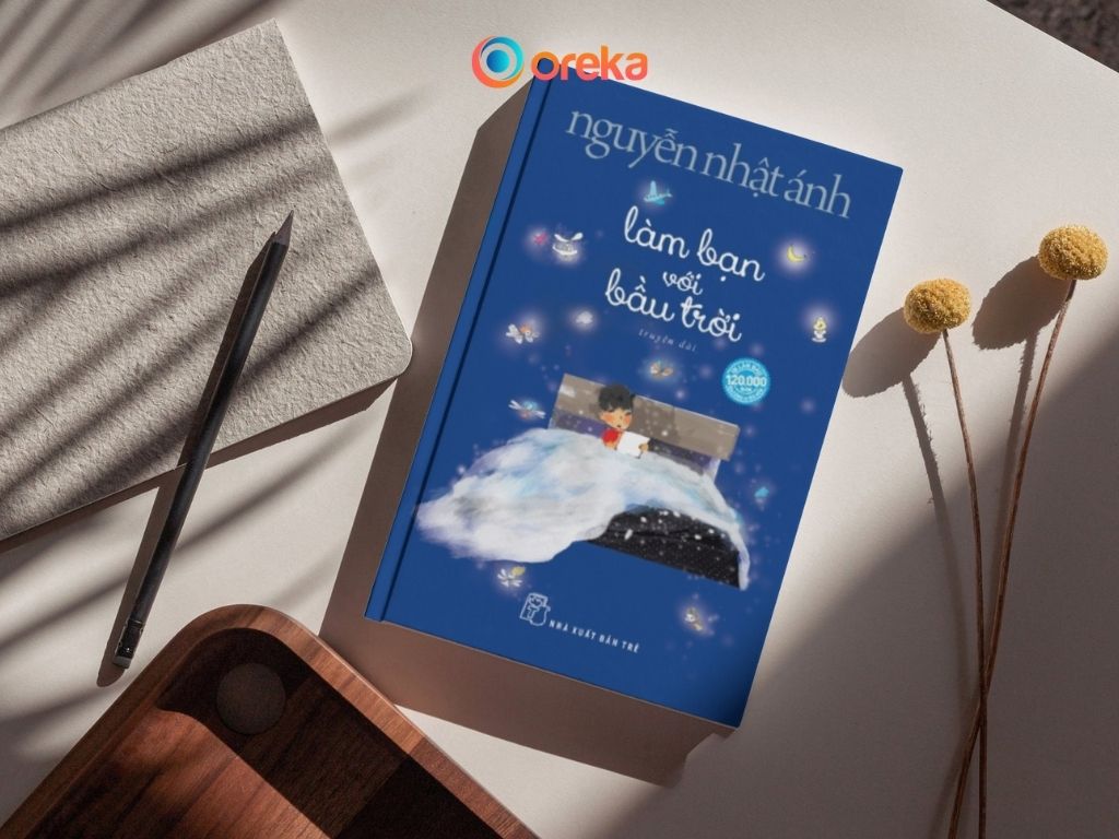 review Làm bạn với bầu trời. Hình ảnh cuốn sách được đặt trên mặt bàn, bên cạnh có 1 cái bút, 1 nửa cuốn sổ, và 1 khay gỗ